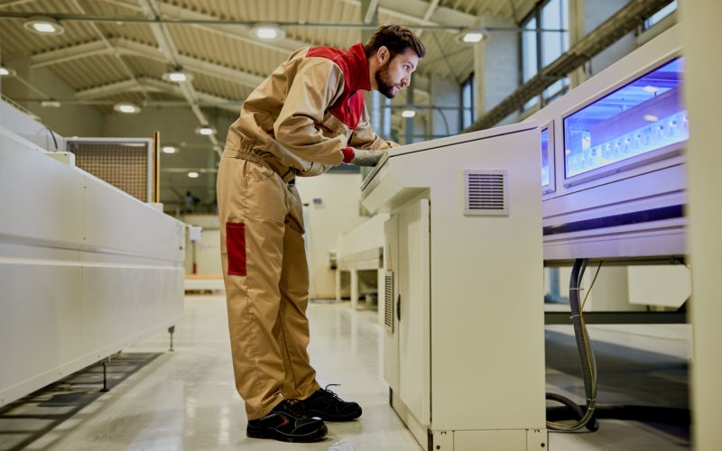 Production line worker operating automated machine at woodworking industrial facility