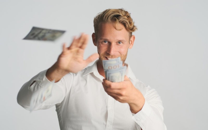 excited blond bearded businessman happily throwing money into camera