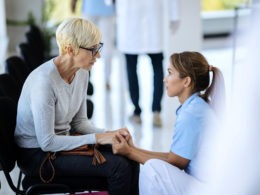 Caring nurse consoling mature woman in waiting room at medical clinic