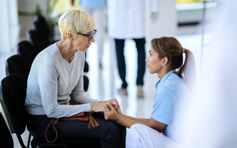 Caring nurse consoling mature woman in waiting room at medical clinic