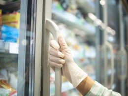 Close up view of hand in protective rubber gloves opening fridge with frozen food in supermarket