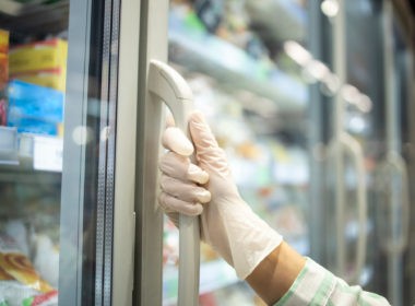 Close up view of hand in protective rubber gloves opening fridge with frozen food in supermarket