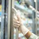 Close up view of hand in protective rubber gloves opening fridge with frozen food in supermarket