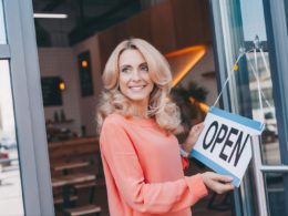 Beautiful happy cafe owner holding sign open and looking away