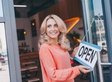 Beautiful happy cafe owner holding sign open and looking away