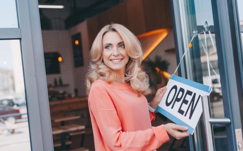 Beautiful happy cafe owner holding sign open and looking away