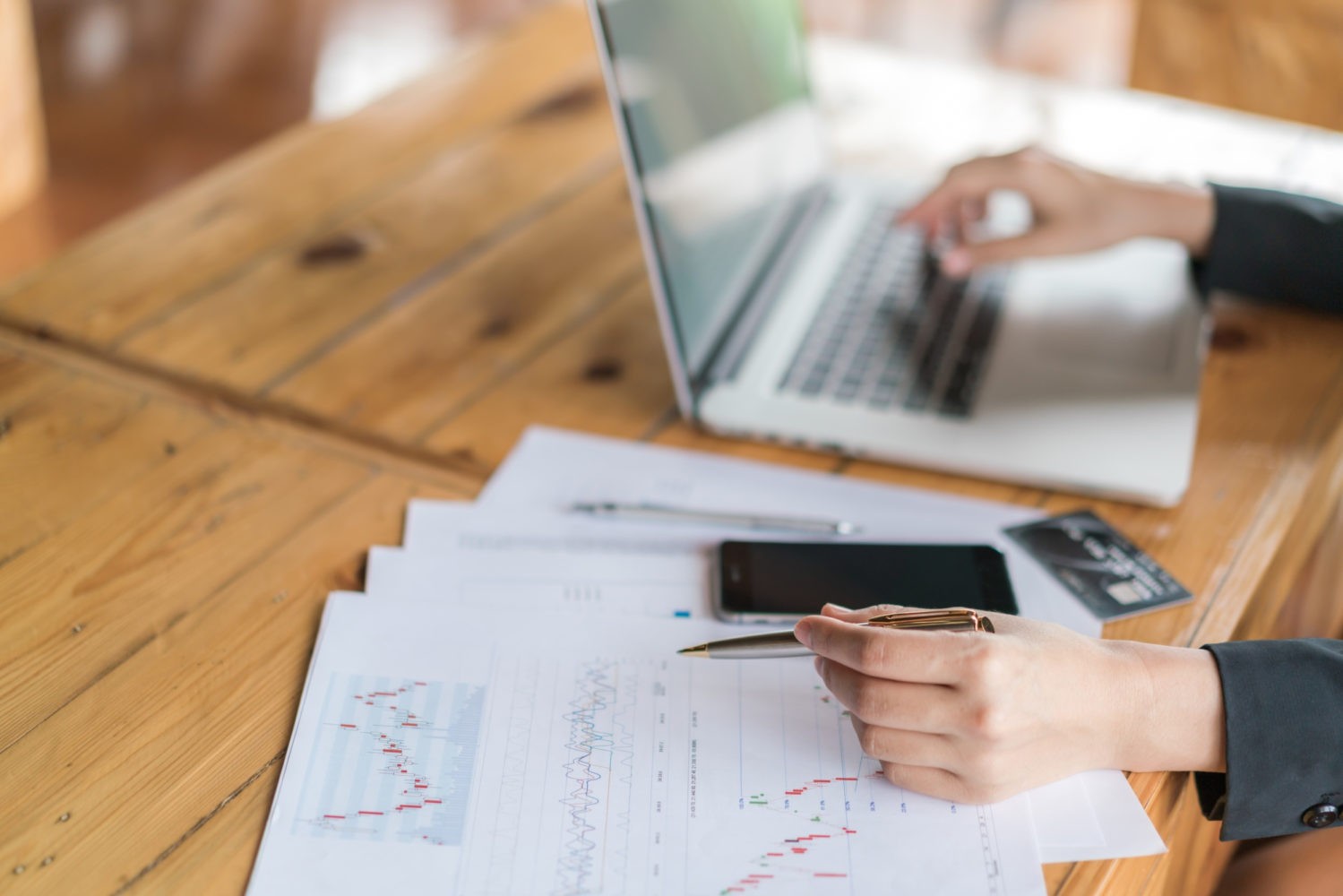 Business woman hand with financial charts and laptop on the table .