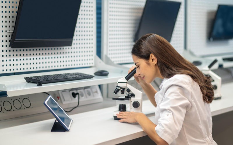 Woman sitting at table looking through microscope