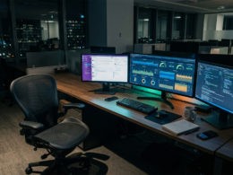 Office desk with active workflow dashboards on screens and no person present, representing autonomous AI operations