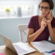 A remote worker sitting at a desk with a laptop open, looking distracted and disengaged